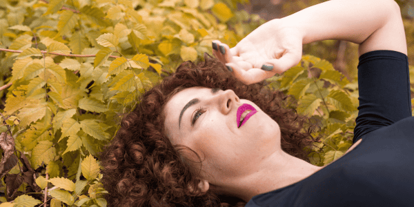 Portrait of a woman with auburn curly hair, displaying a natural expression while resting on a bed of golden yellow autumn leaves